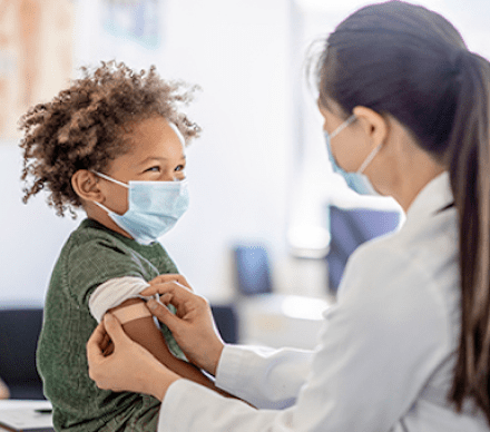 A woman in white coat and mask giving boy vaccine.
