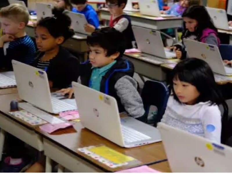 A group of children sitting at desks with laptops.