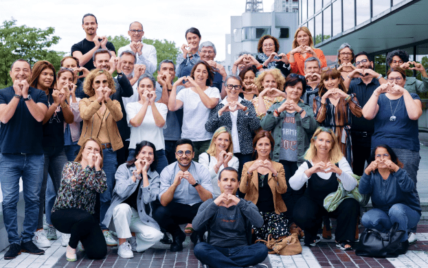 A group of people standing on the sidewalk making heart signs.