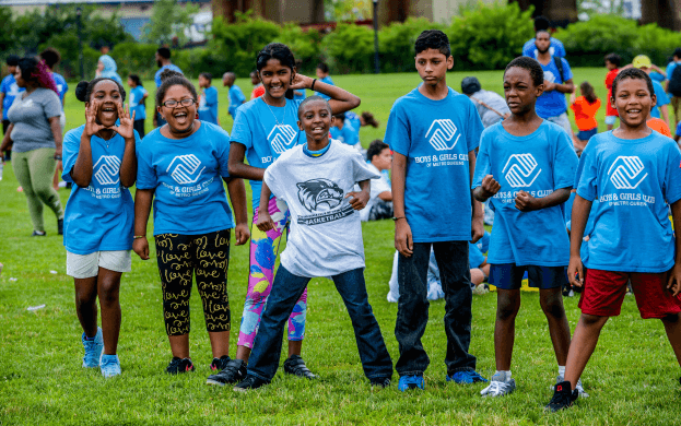A group of children in blue shirts standing on top of a grass covered field.